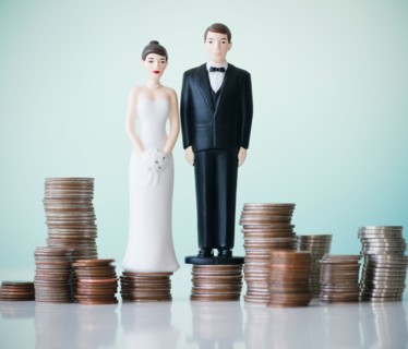 Close up of wedding cake figurines on stacks of coins. Photo : Jamie Grill