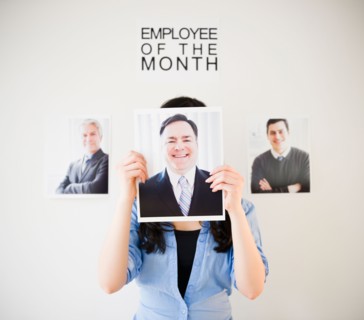 Businesswoman holding photos of men to her face. Photo : Jamie Grill