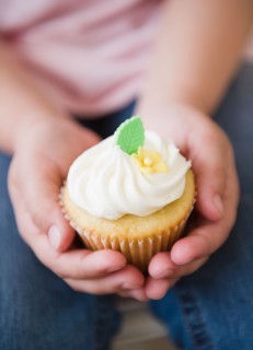 Close up of girl's (8-9) hands holding cupcake. Photo : Jamie Grill