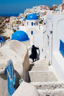 Greece, Cyclades Islands, Santorini, Oia, Woman descending steps past traditional buildings.