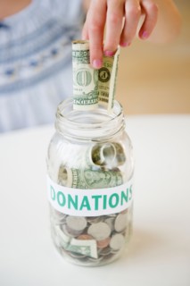 Close up of girl's (10-11) hand putting dollar bill into jar. Photo: Jamie Grill