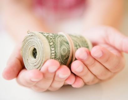 Close up of girl's (8-9) hands holding money roll. Photo: Jamie Grill