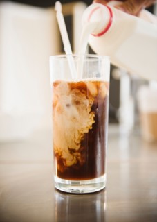 Close up of hand pouring milk into iced coffee. Photo : Jamie Grill