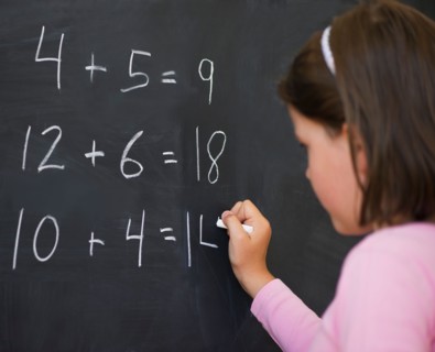 Close up of girl (6-7) writing on blackboard. Photo : Daniel Grill