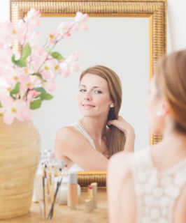 Young woman brushing hair in front of mirror. Photo : Daniel Grill