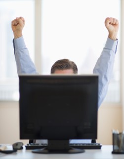 Businessman raising hands from behind computer.