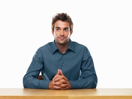 Smiling business man sitting at table with hands clasped. Photo : momentimages