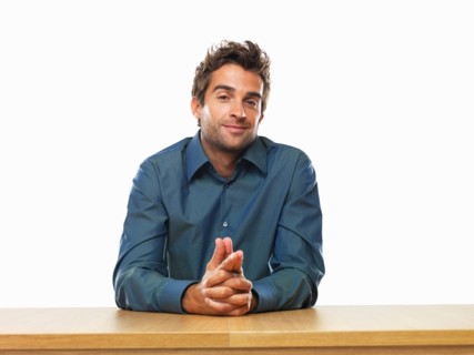Smiling business man sitting at table with hands clasped. Photo : momentimages
