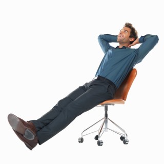 Studio shot of young man relaxing on chair with hands behind head. Photo : momentimages