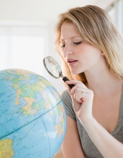 Young woman with magnifying glass searching on globe. Photo : Jamie Grill