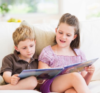 Close up of girl (6-7) and boy (4-5) reading book on sofa. Photo : Daniel Grill