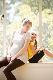Daughter (6-7) sitting back to back with pregnant mother, embracing. Photo : Rob Lewine