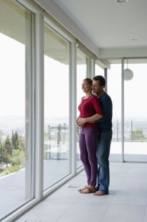 Mature couple in empty living room looking through window. Photo : Rob Lewine