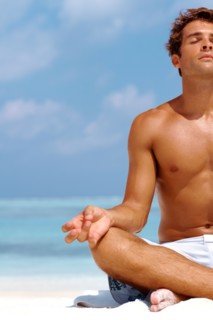 Cropped image of a young man meditating at the beach in a lotus position. Photo : momentimages
