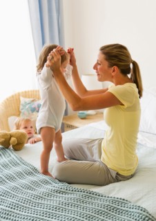 Mother playing with daughter (2-3) on bed.