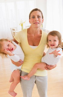 Mother holding crying daughters (2-3) and making facial expression.