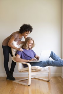 Young woman looking at man using laptop at home. Photo : Rob Lewine