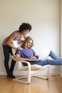 Young woman looking at man using laptop at home. Photo : Rob Lewine