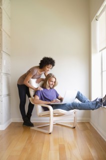Young woman looking at man using laptop at home. Photo : Rob Lewine