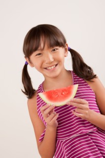 Studio portrait of girl (10-11) eating watermelon. Photo : Rob Lewine