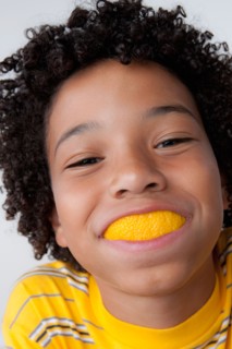 Studio portrait of boy (8-9) with slice of lemon in mouth. Photo : Rob Lewine