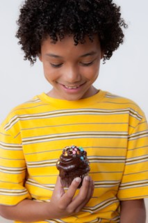 Studio portrait of boy (8-9) holding muffin. Photo : Rob Lewine