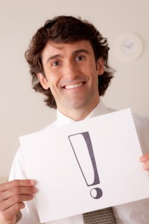 Studio portrait of businessman holding sheet of paper with exclamation mark. Photo : Rob Lewine