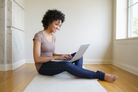 Young woman sitting in room using laptop. Photo : Rob Lewine