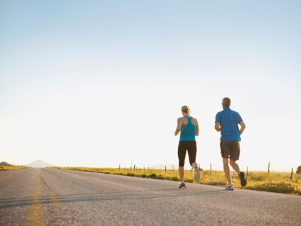 Mid adult couple running on empty road. Photo: Erik Isakson