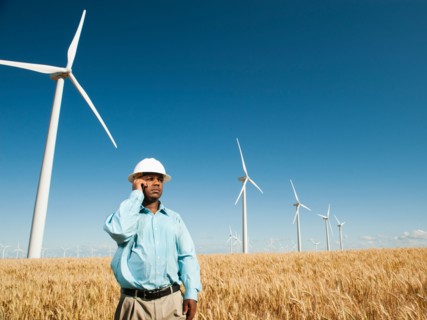 USA, Oregon, Wasco, Engineer standing in wheat field in front of wind turbines, using mobile phone.