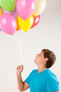 Studio shot of boy (12-13) holding bunch of balloons. Photo : Rob Lewine