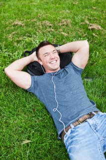 Man lying on grass listening to mp3 player. Photo : Take A Pix Media