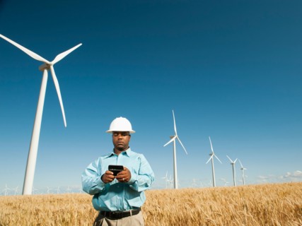USA, Oregon, Wasco, Engineer standing in wheat field in front of wind turbines, using mobile phone.