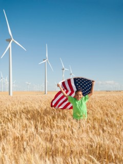 USA, Oregon, Wasco, Boy (8-9) flying american flag in wheat field with wind turbines in background.