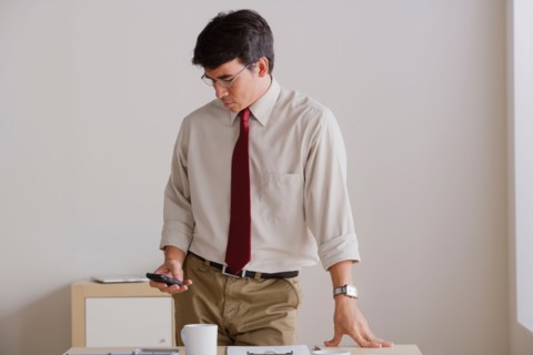 Businessman using cell phone in office. Photo: Rob Lewine