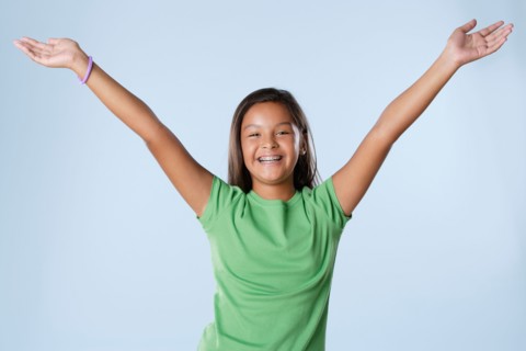 Studio portrait of girl smiling (10-11) with raised hands. Photo : Rob Lewine