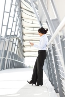 Young businesswoman on walkway, using cell phone. Photo: Take A Pix Media