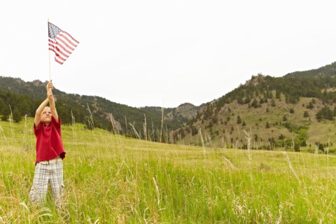 Boy (6-7) waving American flag in meadow. Photo : Shawn O'Connor