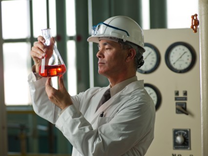 Worker in lab coat examining liquid in beaker. Photo : db2stock