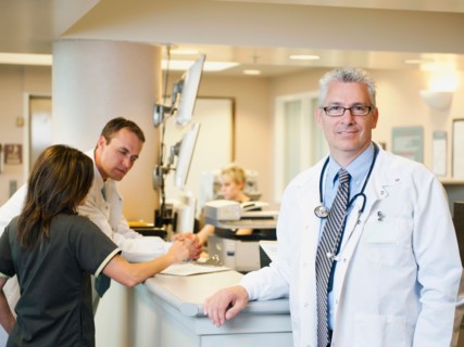 Portrait of confident doctor with two colleagues working in background.