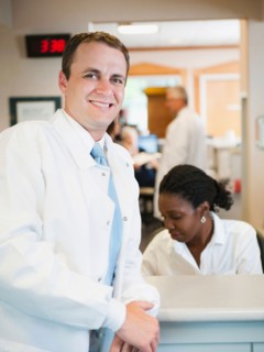 Portrait of doctor with hospital receptionist working in background. Photo: Erik Isakson