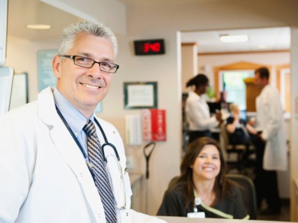 Portrait of confident doctor with female nurse in background.