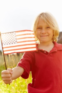 Portrait of boy (6-7) waving American flag in meadow. Photo : Shawn O'Connor