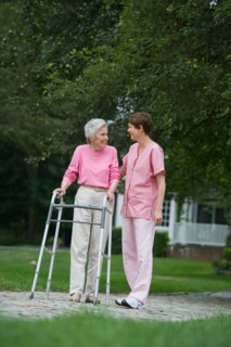 Senior woman walking with walker with help of nursing assistant.