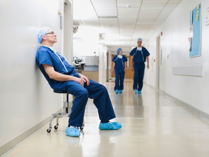 Surgeon resting in hospital corridor after operation, while two of his colleagues are walking in