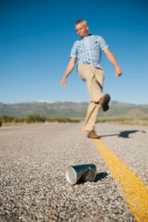 Man kicking tin can on otherwise empty road.
