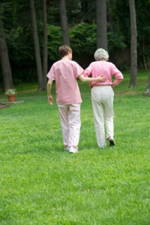 Senior woman and nursing assistant walking in back yard.