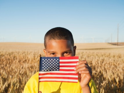 Boy (8-9) holding a small American flag in wheat field.