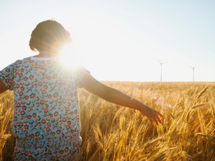 Girl (10-11) walking in glorious sunshine amidst wheat.