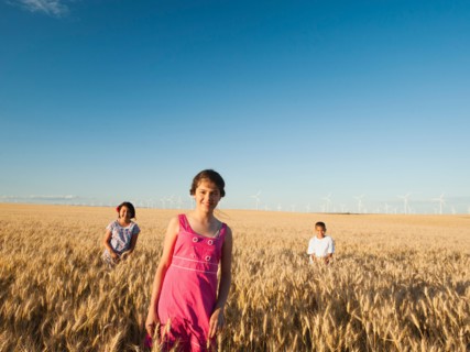 Girls (10-11, 12-13) and boy (8-9) standing in wheat field.